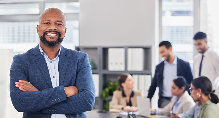 man smiling with arms folded while his team works behind him